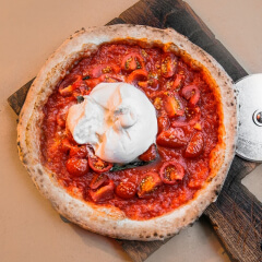 Pizza con borde inflado, cubierta de salsa de tomate, tomates cherry y una bola de burrata en el centro, sobre tabla de madera.